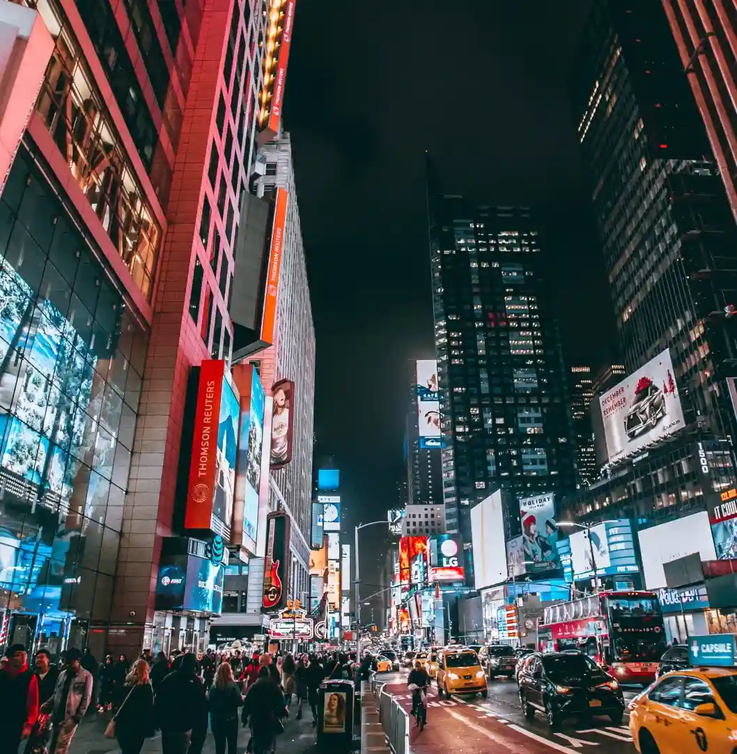 Times Square at night, illuminated by neon lights and advertisements, with taxis and pedestrians in view.