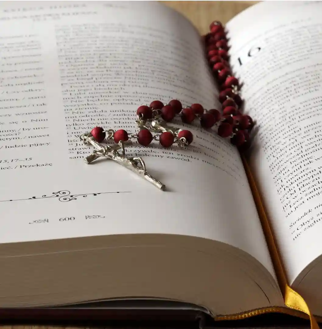 A close-up of a rosary placed on an open book, with the pages displaying text in the background.